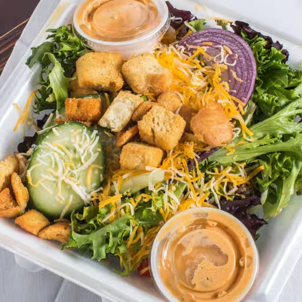 Fresh garden salad with mixed greens, red onion, cucumber, shredded cheese, croutons, and two dressings.