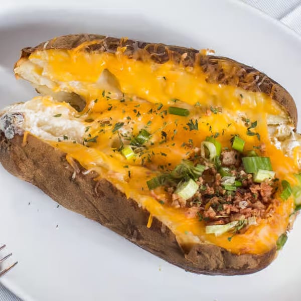 A loaded baked potato with melted cheese, bacon bits, and green onions on a white plate.