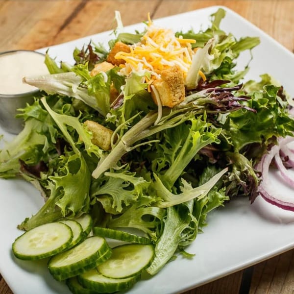 Fresh garden salad with mixed greens, shredded cheese, croutons, cucumber slices, and red onion.