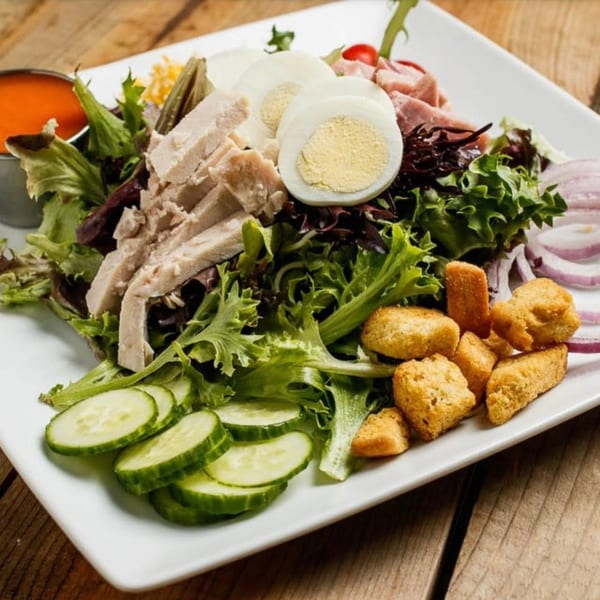 A chef salad with chicken, ham, hard-boiled eggs, cucumbers, croutons, and red onions.