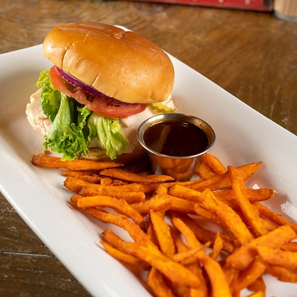 Turkey sandwich with lettuce, tomato, and onion, served with sweet potato fries and a side of au jus.